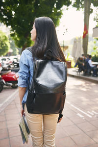Rear view of woman with backpack standing on footpath