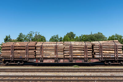 Stack of firewood by plants against clear blue sky