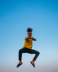 Low angle view portrait of young woman against clear blue sky