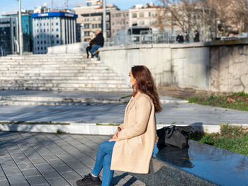 Woman wearing mask looking away sitting against tree