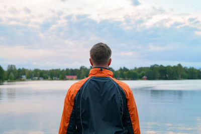 Rear view of man looking at lake against sky