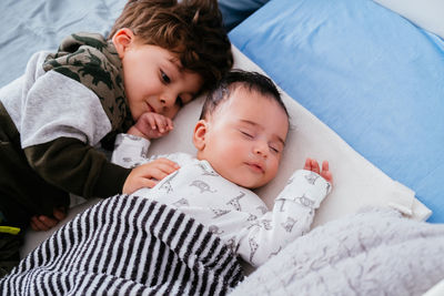 From above of charming little boy embracing little sibling while sleeping peacefully together in cozy bed