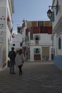 Rear view of people walking on street amidst buildings in city