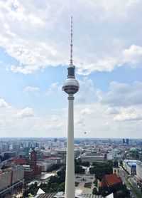 Communications tower in city against cloudy sky