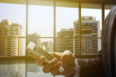 Cropped image of businessman using mobile phone in office during sunset
