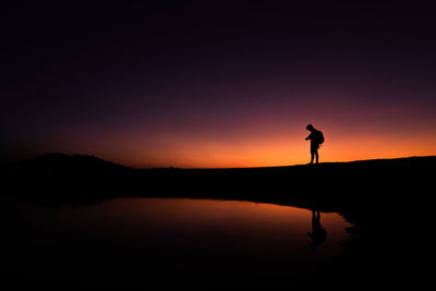 Silhouette man standing by lake against sky during sunset