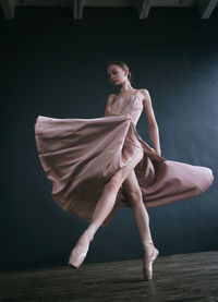 A ballerina in a pink dress and punts moves around the room with a fluttering dress