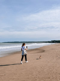 Rear view of woman standing at beach against sky