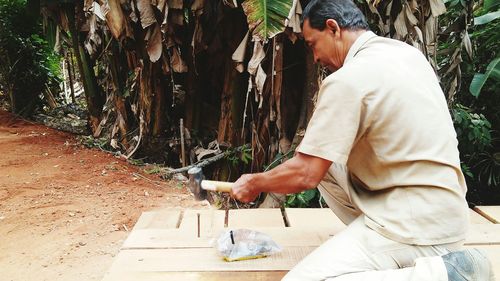 Carpenter hitting nail on wooden planks against trees