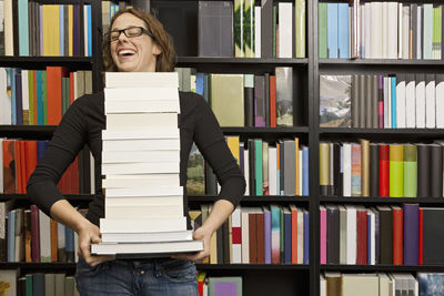 Woman carrying stack of books in bookstore