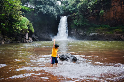 Rear view of boy standing against waterfall