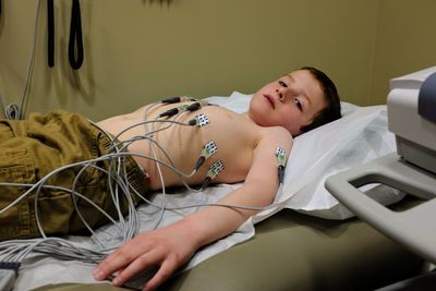 Shirtless boy with medical equipment on chest lying at bed in hospital