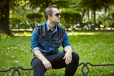 Young man looking away while sitting on grass