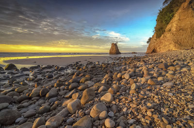 Pebbles on beach against sky during sunset