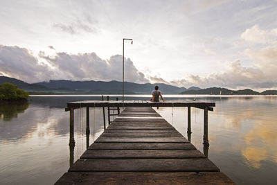 Rear view of man sitting on pier over lake