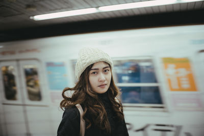 Portrait of young woman wearing knit hat at railroad station at night