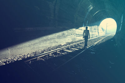 Rear view of man walking on railroad tracks in tunnel