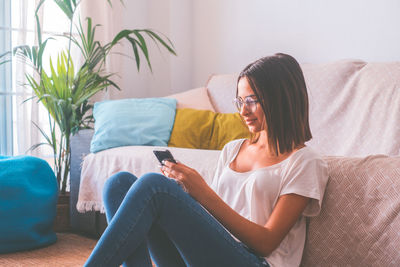 Side view of young woman using digital tablet while sitting on sofa at home