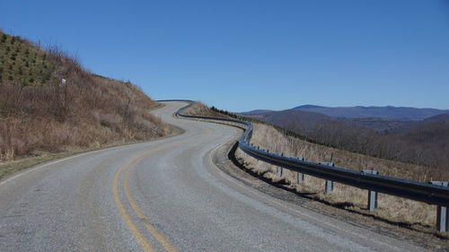 Road leading towards mountain against clear blue sky