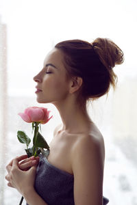 Portrait of a beautiful attractive woman in a gray towel in the bathroom holding a red rose