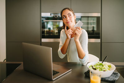 Young woman using phone while sitting on table