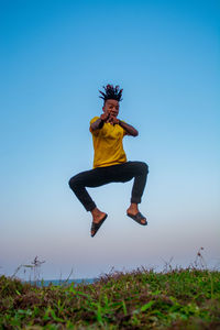 Full length of young woman jumping on field against clear sky