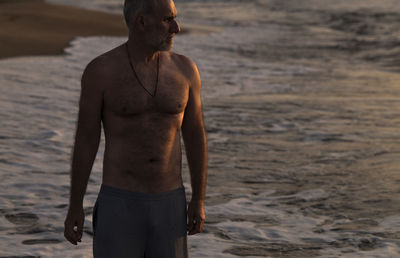 Portrait of shirtless adult man on beach during sunrise