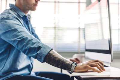 Midsection of man using computer on table in office