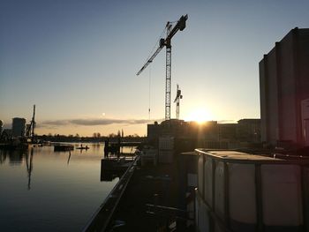 Cranes in city against clear sky during sunset