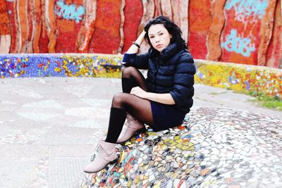 Young woman looking away while sitting on wall