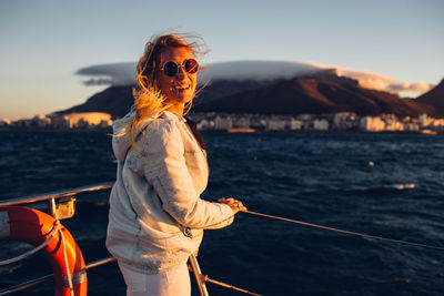 Man wearing sunglasses standing by boat against sky during sunset