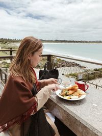 Side view of young woman having food while sitting outdoors