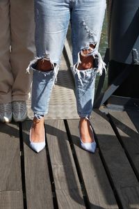 Legs of a woman standing on a jetty, wearing distressed jeans, with her partner beside her.