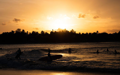 Silhouette people by sea against sky during sunset