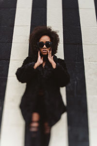 Portrait of young woman wearing sunglasses standing against wall