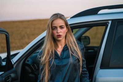 Portrait of young woman with long hair standing by car