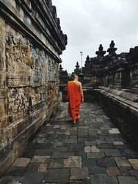 Rear view of monk walking on footpath by temple against sky