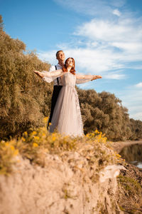 A young wedding couple in love on the edge of a cliff against the backdrop of the river and the sky.