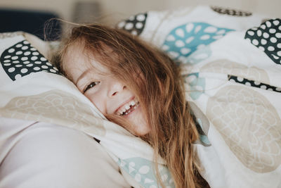 Smiling girl wrapped in blanket on bed at home