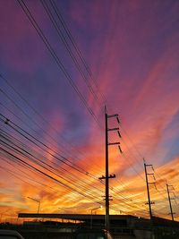 Low angle view of electricity pylon against orange sky