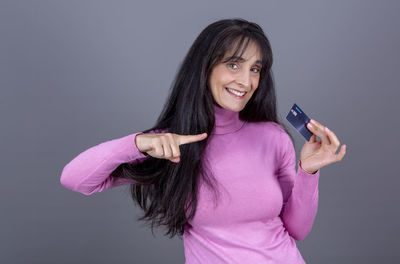 Beautiful long-haired brunette woman in her 40s, smiling and showing her credit card.