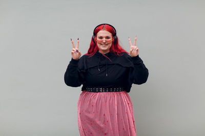 Portrait of young woman with arms raised standing against white background