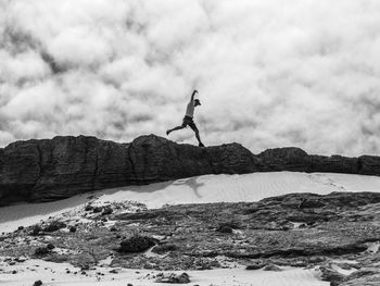 Side view of mid adult man jumping on rocks against cloudy sky