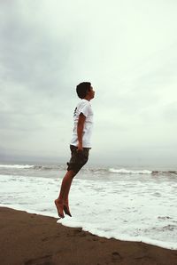 Side view of man jumping at beach against sky