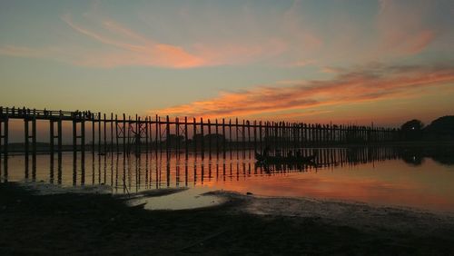 Silhouette wooden posts on beach against sky during sunset