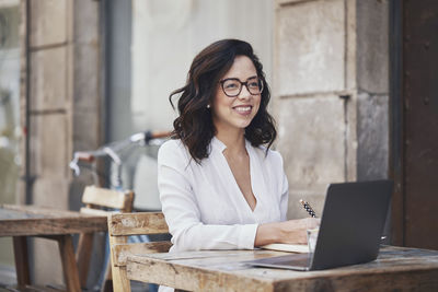 Smiling businesswoman writing in diary while sitting at sidewalk cafe