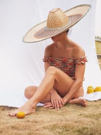 Woman wearing hat sitting on land by curtain