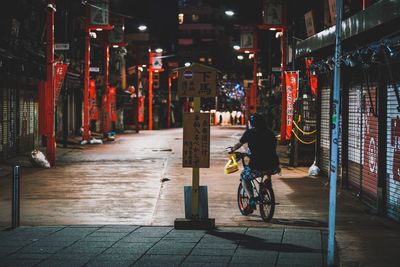 Rear view of man cycling on illuminated city at night