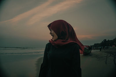 Woman wearing hijab enjoying at beach against sky during sunset
