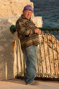 Side view of mature man standing by rusty railing on sunny day